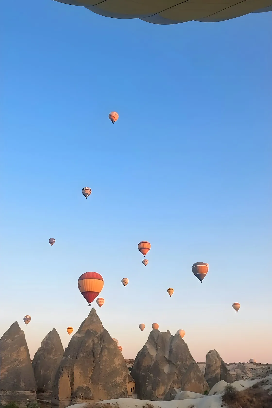 Hot air balloons rising over the rock formations of Cappadocia, Turkey, at sunrise, seen from a balloon basket.